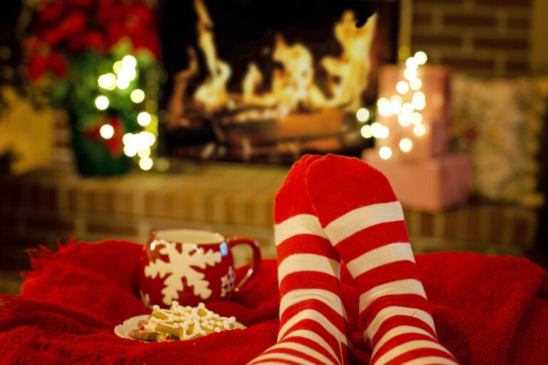 Foto nohou ve vánočních pruhovaných ponožkách před krbem s vánoční atmosférou